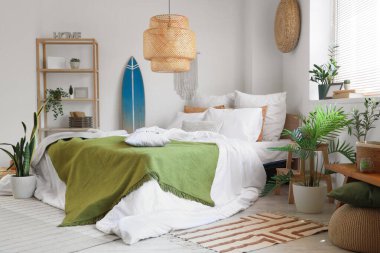 Büyük rahat bir yatak, raf ünitesi, sörf tahtası ve yatak odasının iç kısımlarında bitkiler.