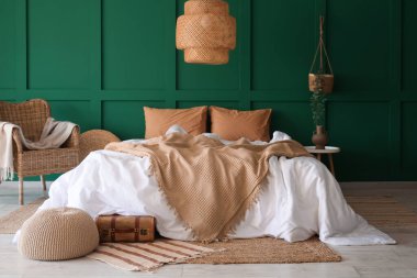 Büyük rahat bir yatak, koltuk, komodin ve yatak odasının içinde bavulun yanında puf.