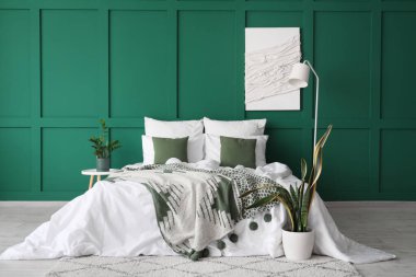 Yatak odasının içinde büyük rahat bir yatak, lamba ve bitkiler var.