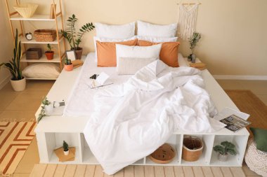 Yatak odasının içinde kırışık çarşaflar ve raf üniteleri olan büyük, rahat bir yatak.