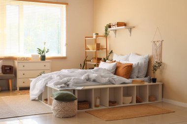 Büyük konforlu yatak, ev bitkileri, çekmeceler ve yatak odasının içindeki raf üniteleri.