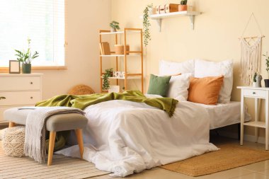 Buruşuk çarşaflı, raflı, komodinli ve yatak odasının içindeki banklı büyük, rahat bir yatak.