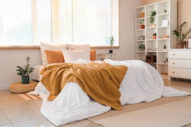 Buruşuk çarşaflı, komodinli, raf üniteli, çekmeceli ve yatak odasındaki çiçekli büyük rahat bir yatak.