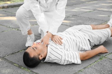 Kadın doktor parkta kalp krizi geçiren baygın bir adama kalp masajı yapıyor.