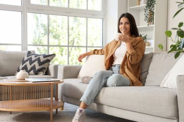 Sabahları elinde kahve olan güzel bir kadın evdeki kanepede oturuyor.