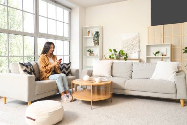 Sabahları evdeki koltukta cep telefonu kullanan güzel bir kadın.