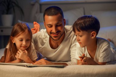 Baba, küçük çocukları için evde masal okuyor.