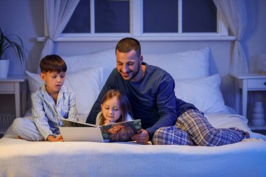 Genç baba evde sevimli çocuklar için masal okuyor.