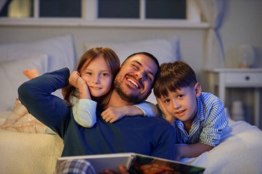 Baba yatak odasında çocuklarına masal okuyor.