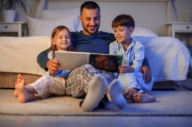 Baba ve küçük çocukları yatak odasında masal okuyorlar.