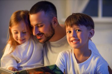 Baba ve küçük çocuklar uyumadan önce masal okuyorlar.