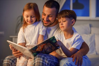 Baba yatak odasında çocukları için kitap okuyor.
