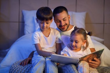 Mutlu baba ve sevimli küçük çocukları evde masal okuyorlar.