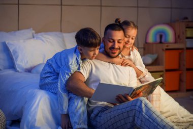 Mutlu baba ve sevimli küçük çocukları evde masal okuyorlar.