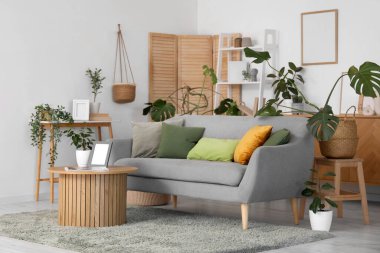 Kanepe, masa ve yeşil bitkilerle aydınlık oturma odasının içinde.