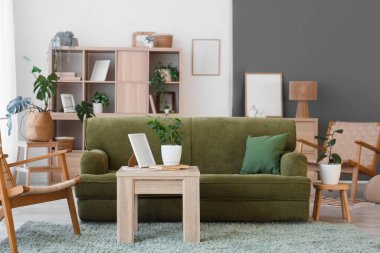 Oturma odasının içinde yeşil kanepe, koltuk ve bitkiler var.