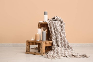 Odasında bej duvarın yanında yanan mumlar ve ekoseli tahta kutular var.