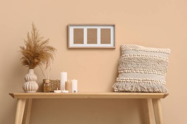 Çimenli vazo, yanan mumlar ve odada bej duvarın yanındaki masada yastık.