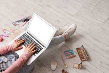 Hafif ahşap zeminde dizüstü bilgisayar ve makyaj ürünleri kullanan kadın güzellik blogcusu