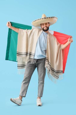 Mavi arka planda Meksika bayrağı olan şapkalı yakışıklı bir adam.