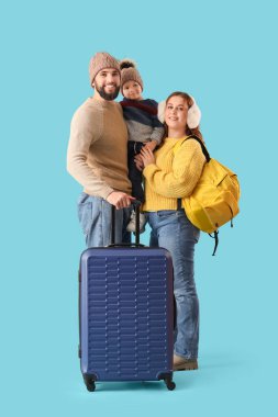 Mutlu ebeveynler ve küçük oğulları kışlık giysiler ve mavi arka planda çantalar. Seyahat kavramı
