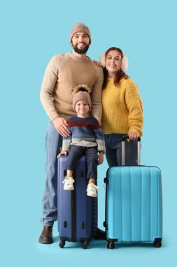 Mutlu ebeveynler ve mavi arka planda küçük oğulları kışlık giysiler ve bavullar. Seyahat kavramı