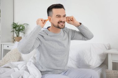 Yakışıklı adam yatak odasına kulak tıkacı koyuyor.