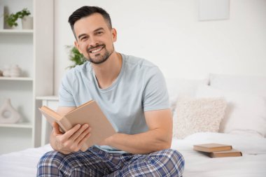 Yatak odasında kitap okuyan yakışıklı bir adam.