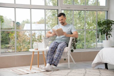 Evdeki koltukta kitap okuyan yakışıklı adam.