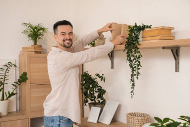 Yakışıklı adam evdeki raftan kitap alıyor.