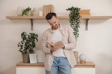 Evde klozetin yanında kitap okuyan yakışıklı bir adam.