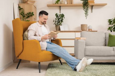 Evdeki koltukta kitap okuyan yakışıklı adam.