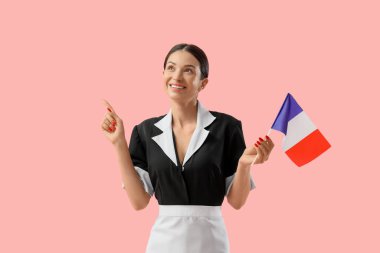 Fransız bayrağıyla genç oda hizmetçisi pembe arka plandaki bir şeyi işaret ediyor.