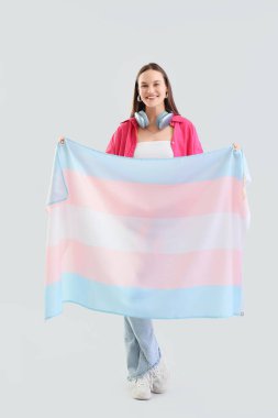 Young woman with transgender flag on light background