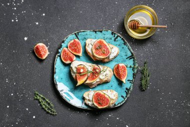 Lezzetli incirli bruschetta tabağı ricotta peyniri ve siyah arka planda bir kase bal