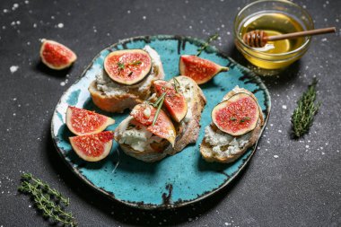 Lezzetli incirli bruschetta tabağı ricotta peyniri ve siyah arka planda bir kase bal