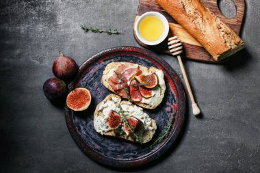 Lezzetli incirli bruschetta tabağı ricotta peyniri ve siyah arka planda bir kase bal