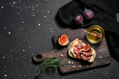 Siyah arka planda prosciutto ve ricotta peynirli lezzetli incirli bruschetta tahtası.