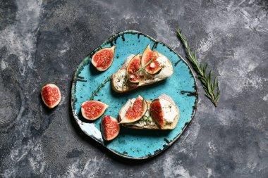 Siyah zemin üzerinde ricotta peyniri ve biberiyeli lezzetli incirli bruschetta tabağı.