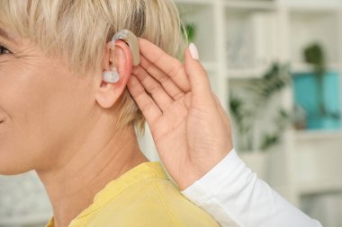 Doktor klinikte yetişkin bir kadının kulağına işitme cihazı takıyor.