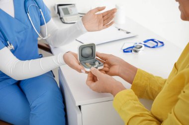Doktor klinikte yetişkin kadınlara işitme cihazı veriyor.