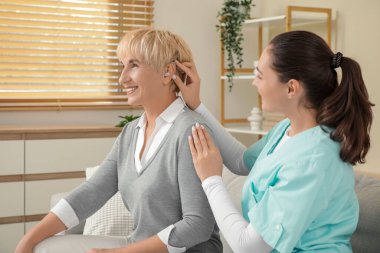 Doktor evde onu ziyaret ederken yetişkin bir kadının kulağına işitme cihazı takıyor.