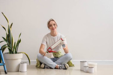 Odada ışık duvarının yanında oturan dolgu macunlu genç kadın.