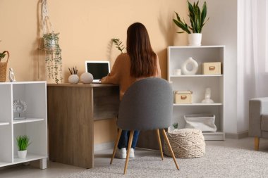 Yeşil duvarın yanında modern dizüstü bilgisayarla çalışan genç bir kadın.