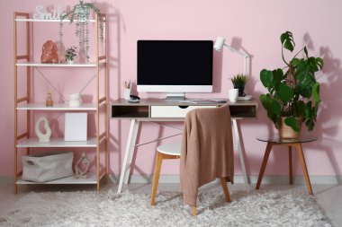 Pembe duvarın yanında bilgisayar ve kırtasiye malzemesi olan modern bir işyeri.