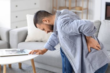 Evdeki masanın yanında sırt ağrısı çeken genç bir adam.