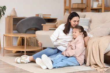 İşitme cihazı olan küçük bir kız ve annesi evde dizüstü bilgisayardan çizgi film izliyor.