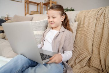 İşitme cihazlı küçük bir kız evde dizüstü bilgisayar izliyor.