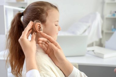 Kadın doktor hastanede küçük kızın kulağına işitme cihazı takıyor.