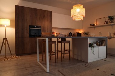 Akşam vakti mutfak masası, tezgahlar ve parlayan lambalar.